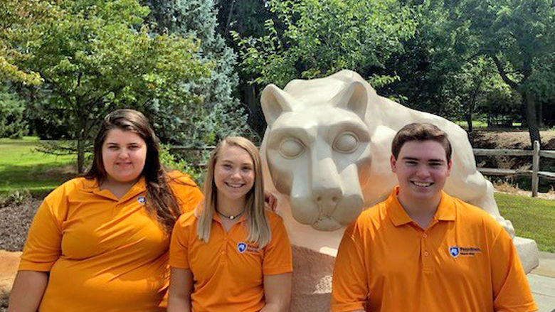 Three students in orange shirts sit together at Lion Shrine