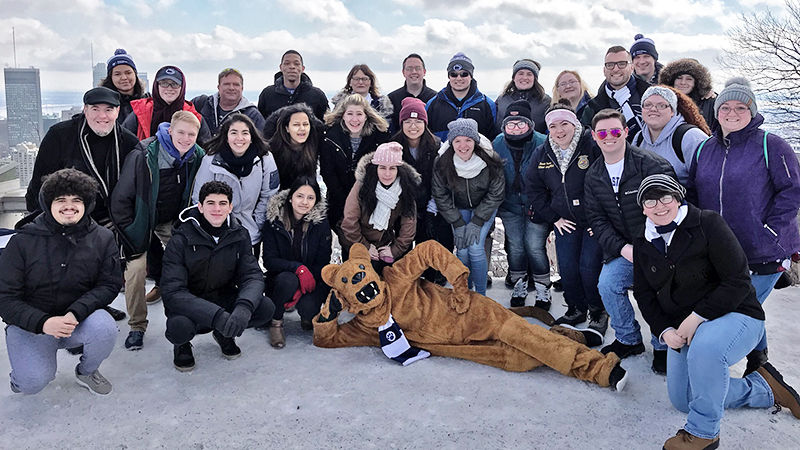 Group of Penn State students and chaperones pose in a lofty patio area overlooking Montreal