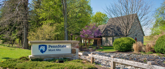 Penn State Mont Alto sign surrounding by a bright green garden situated in front of a small cottage.