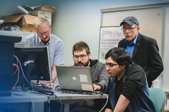 Two students and two professors collaborating on a project in a technology lab