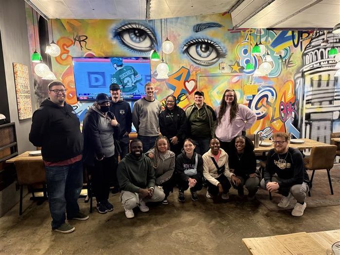 A group of students pose for a photo in front of a mural.