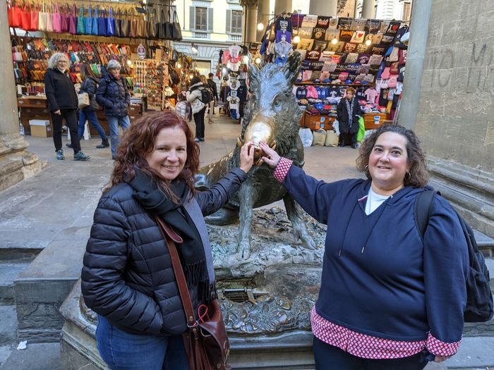 Two women pose in front of a pig statue in Florence, Italy