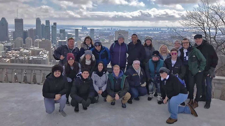 Group of Penn State students and chaperones pose in a lofty patio area overlooking Montreal