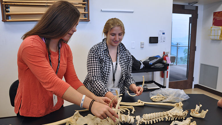 Two female high school students examine a skeleton on a table