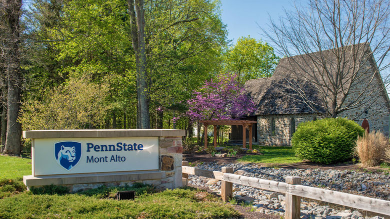 Penn State Mont Alto sign surrounding by a bright green garden situated in front of a small cottage.