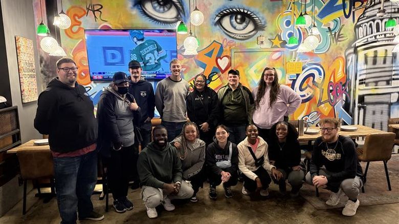 A group of students pose for a photo in front of a mural.