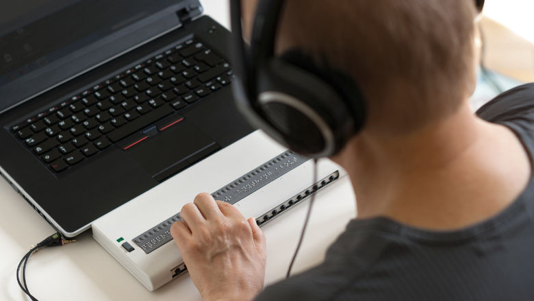 Person using a computer with Braille display and headphones