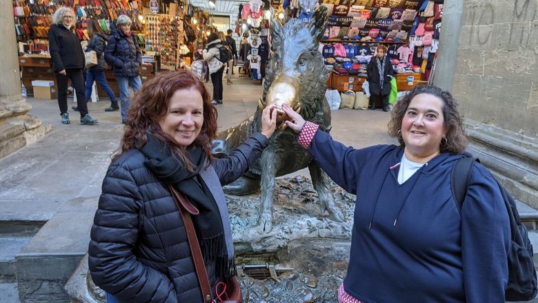 Two women pose in front of a pig statue in Florence, Italy