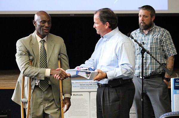 Chancellor Francis Achampong hands the WCHS project policies and procedures book to WCHS President Greg Duffey.