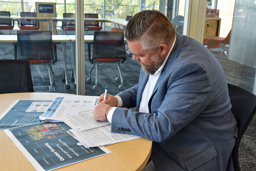 Man in a suit at a table writing on documents.