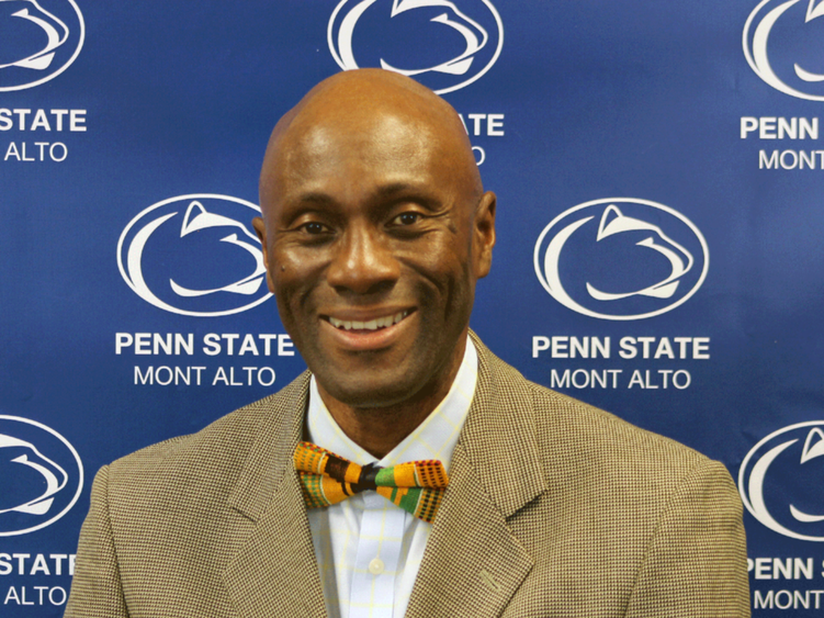 Photo of Francis Achampong in a tie and jacket in front of a blue Penn State backdrop.