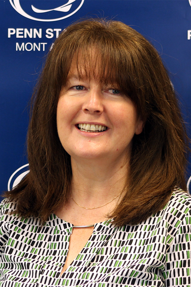 Woman with brown hair in front of blue Penn State background
