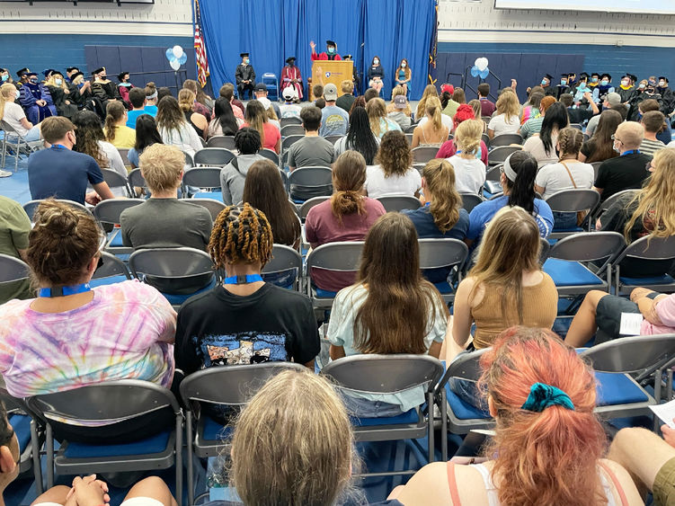 Students seated in gym listening to speaker at podium 