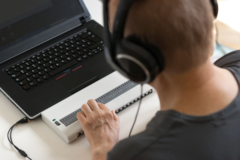 Person using a computer with Braille display and headphones